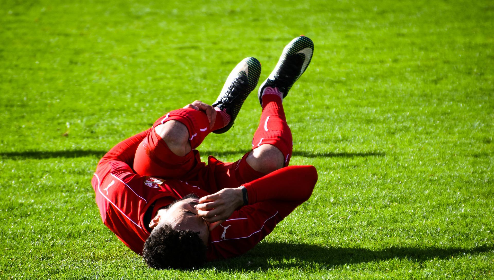 A football player in red writes in agony on the green grass