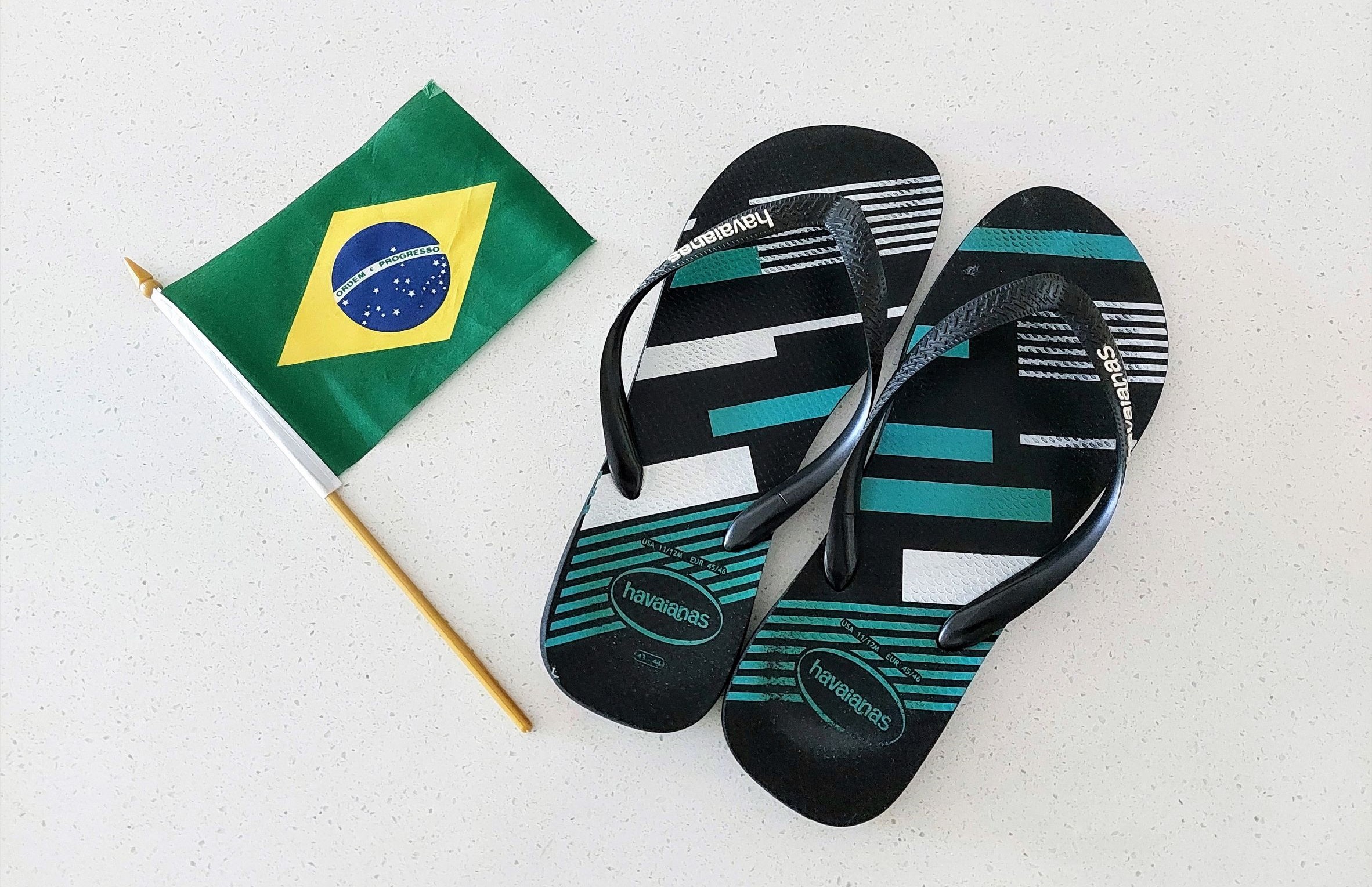 A Brazilian flag on a stick next to a multicoloured pair of Havianas shoes.