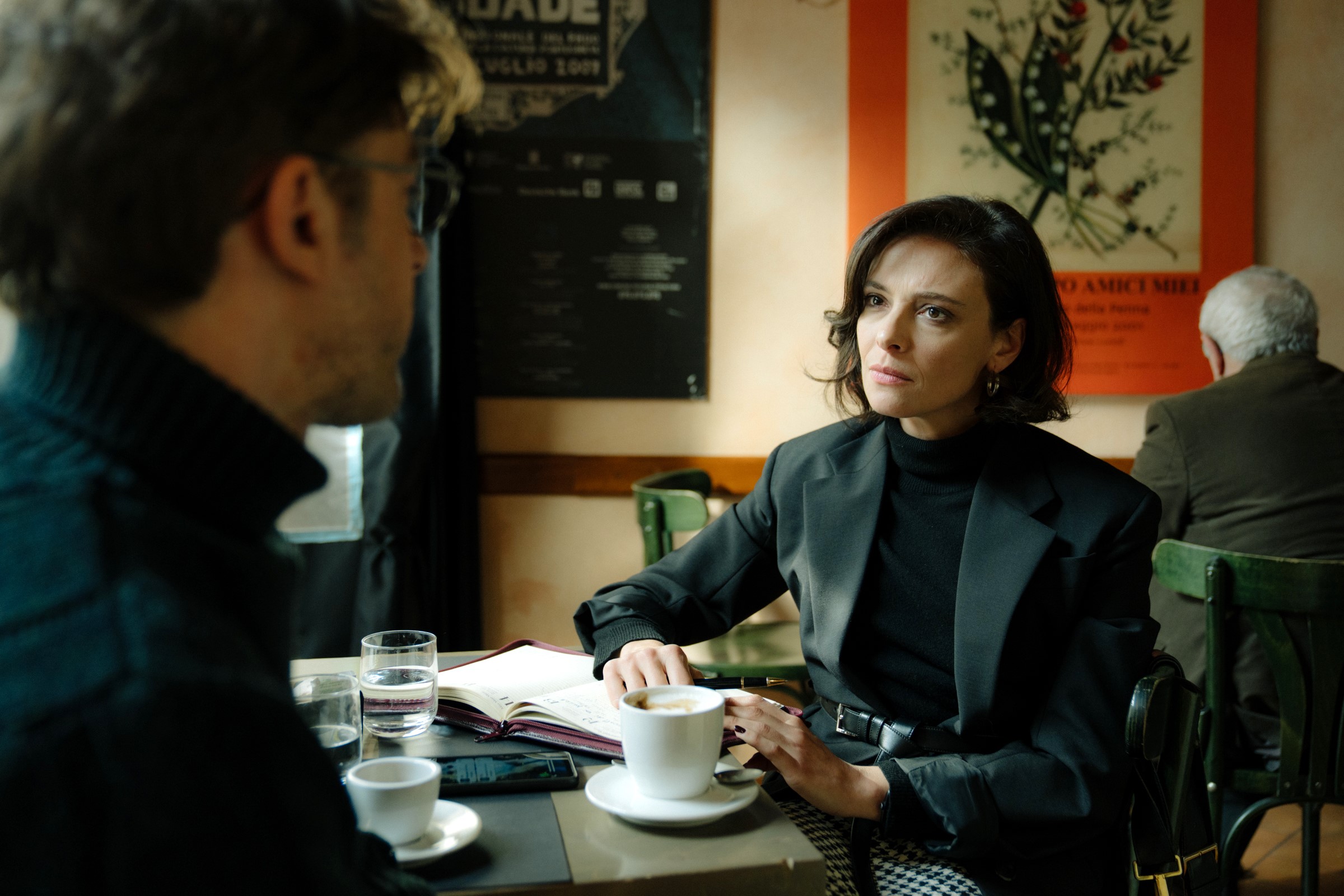 A stern-looking woman behind a desk studies a male colleague.